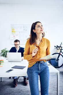 Businesswoman holding tablet in office with colleague in background - BSZF01044