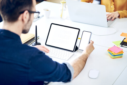 Geschäftsmann arbeitet mit Smartphone und Tablet am Schreibtisch im Büro - BSZF01050