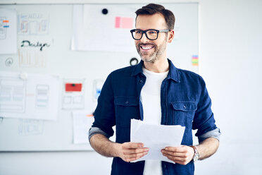 Smiling businessman with papers standing at whiteboard leading a presentation - BSZF01053