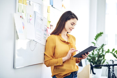 Lächelnde Geschäftsfrau mit Tablet am Whiteboard im Büro - BSZF01056