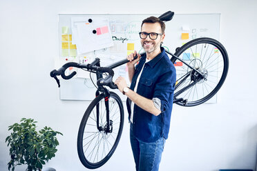 Porträt eines lächelnden Geschäftsmannes mit Fahrrad im Büro - BSZF01059