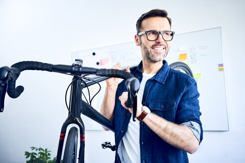Lächelnder Geschäftsmann mit Fahrrad im Büro - BSZF01060