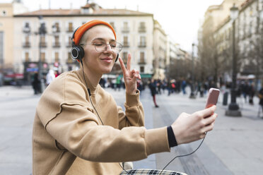 Junge Frau, die ein Selfie macht, während sie Musik hört und mit ihrer Hand eine Friedensgeste macht - WPEF01365