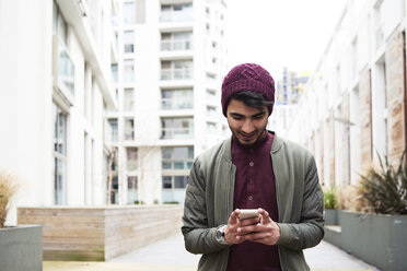 Portrait of cheerful bearded man in purple hat using his mobile phone - IGGF00886