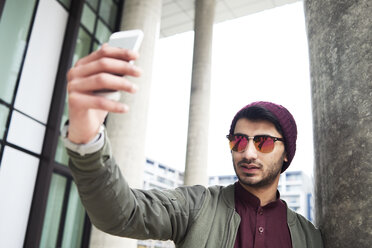 Portrait of stylish man with sunglasses and purple hat taking selfie via mobile phone - IGGF00893