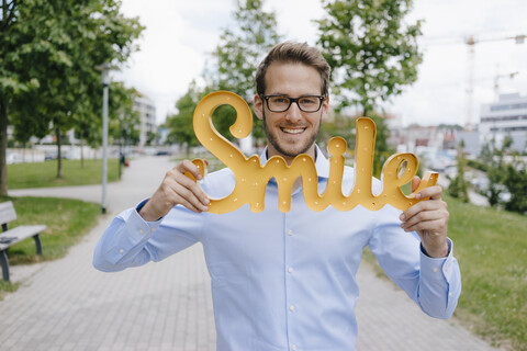 Junger Geschäftsmann hält Lächeln Zeichen, lizenzfreies Stockfoto