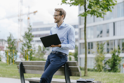 Young businessman sitting on park bench, using laptop stock photo