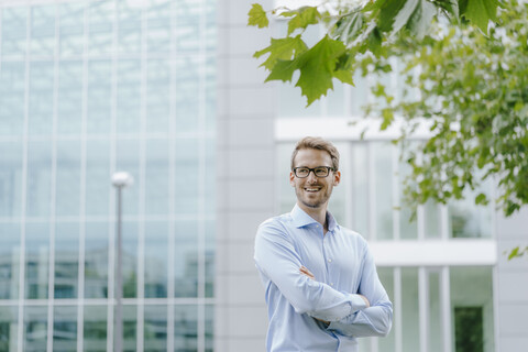 Junger Geschäftsmann steht vor einem modernen Bürogebäude, mit verschränkten Armen, lizenzfreies Stockfoto