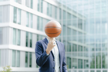 Young businessman standing in front of modern office building, balancing ball on his finger - KNSF05590