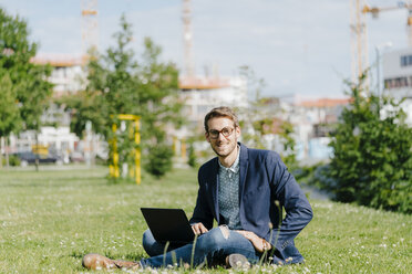 Young businessman sitting in park, using laptop - KNSF05593