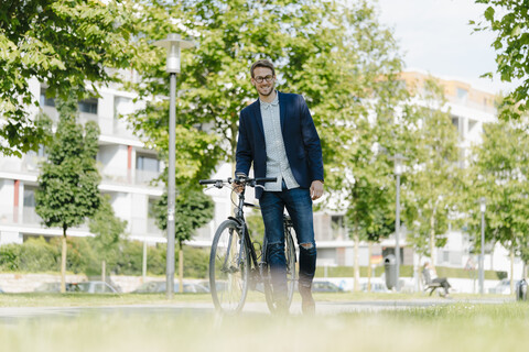Junger Geschäftsmann im Park, der sich auf sein Fahrrad stützt, lizenzfreies Stockfoto
