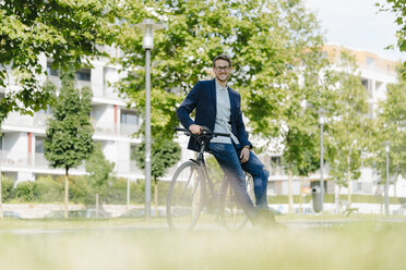 Junger Geschäftsmann im Park, der sich auf sein Fahrrad stützt - KNSF05595