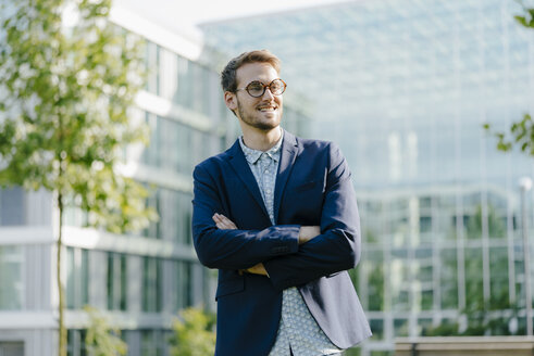 Young businessman standing in front of modern office building, with arms crossed - KNSF05596