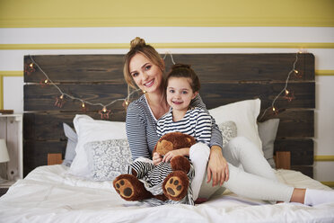 Mother and daighter sitting on bed, girl honding teddy bear - ABIF01180