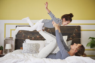 Mother and daughter playing on bed, pretending to fly - ABIF01189