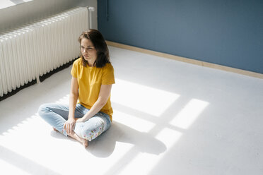 Pensive woman sitting in sunlight cross-legged on floor - KNSF05625