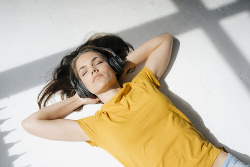 Frau liegt auf dem Boden, entspannt sich im Sonnenlicht, hört Musik - KNSF05632