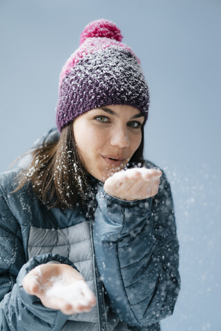 Frau mit Wollmütze, die Schnee bläst, lizenzfreies Stockfoto