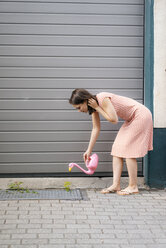 Woman watering plants with a flamingo can in an urban street - KNSF05694