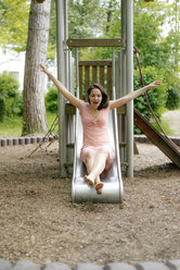 Woman sliding on a slide on a playground - KNSF05704