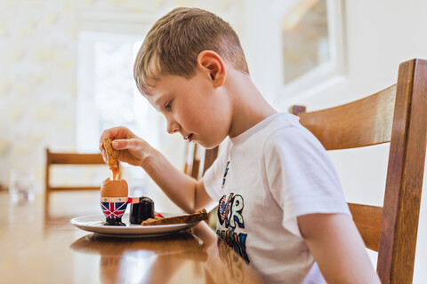 UK, trauriger Junge sitzt am Frühstückstisch und isst ein gekochtes Ei, lizenzfreies Stockfoto