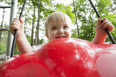 Niedlicher kleiner Junge schwingt auf roter Plastikschaukel auf dem Spielplatz - CAVF60636