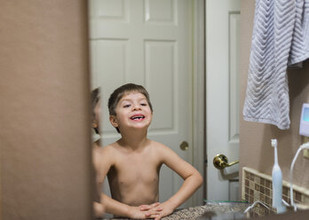 Hemdloser lächelnder Junge mit abgebrochenen Zähnen, der in den Spiegel schaut, während er zu Hause steht - CAVF60644