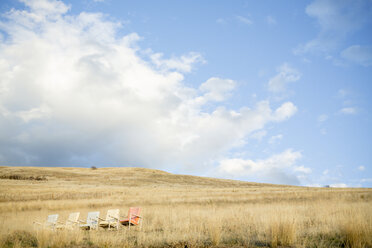 Colorful empty chairs on grassy field against cloudy sky during sunny day - CAVF60652