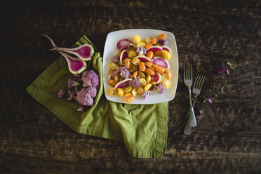 High angle view of salad served in plate with flowers and forks by napkin on wooden table - CAVF60659