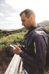 Side view of hiker using smart phone against sky at Wilsons Promontory National Park - CAVF60692