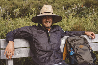 Portrait of smiling hiker with backpack wearing straw hat while sitting on bench at Wilsons Promontory National Park - CAVF60694