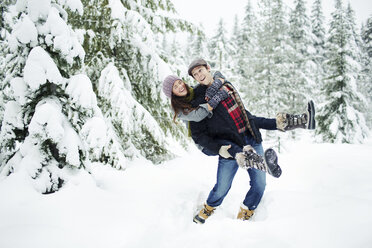 Verspielter Freund nimmt seine Freundin huckepack, während er auf einem schneebedeckten Feld im Wald steht - CAVF60724
