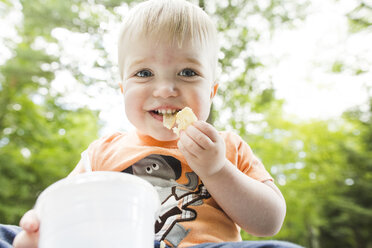 Low angle portrait of cute baby boy eating snacks in park - CAVF60789