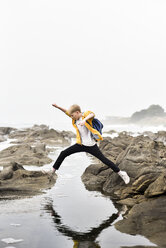 Boy jumping on rocks at beach against clear sky - CAVF60794