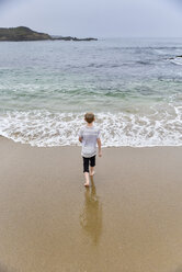 Rear view of boy walking at beach against clear sky - CAVF60795