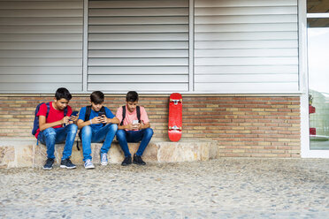 Freunde benutzen Smartphones, während sie vor dem Schulgebäude sitzen - CAVF60852