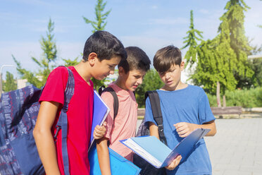 Schoolboys discussing while standing on footpath against sky during sunny day - CAVF60863