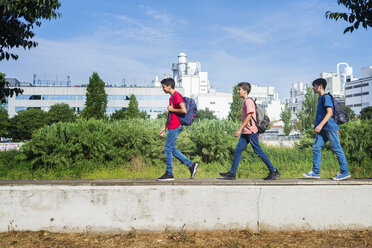 Side view of friends with backpacks walking on retaining wall against sky during sunny day - CAVF60864