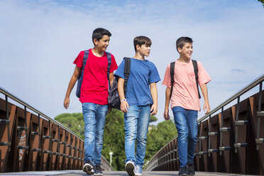 Low angle view of friends with backpacks looking away while walking on footbridge against sky during sunny day - CAVF60871