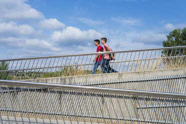 Seitenansicht von Freunden mit Rucksäcken zu Fuß auf dem Steg gegen den blauen Himmel an einem sonnigen Tag - CAVF60878