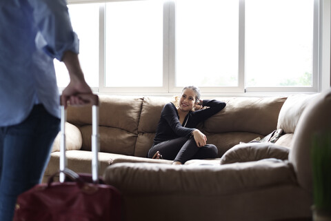 Lächelnde Freundin schaut ihren Freund an, während sie auf dem Sofa in einem Mietshaus sitzt, lizenzfreies Stockfoto