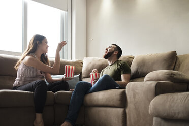 Verspielte Freundin wirft Popcorn in den Mund ihres Freundes, während sie auf dem Sofa in einem Mietshaus sitzt - CAVF60904
