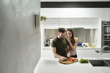 Lächelnder Freund, der in der Küche mit seiner lieben Freundin Tomaten hackt, in einem gemieteten Haus - CAVF60905