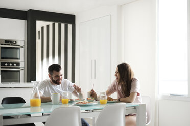 Glückliches junges Paar beim Frühstück am Esstisch in einem Mietshaus - CAVF60906