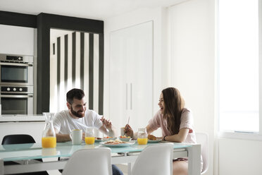 Happy young couple having breakfast at dining table in rental house - CAVF60906