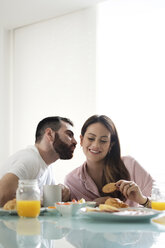 Loving boyfriend kissing girlfriend while having breakfast at dining table in rental house - CAVF60907