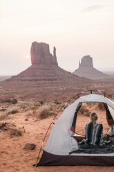 Rear view of woman with scarf sitting in tent at Monument Valley Tribal Park during sunset - CAVF60914