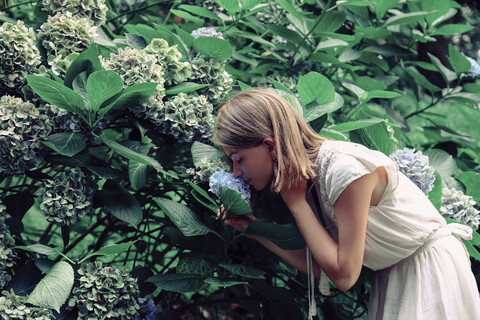 Side view of woman smelling flowers while standing by plants in forest stock photo