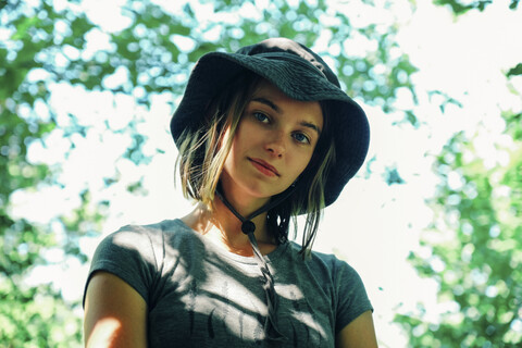 Low angle portrait of woman wearing hat while standing against trees stock photo