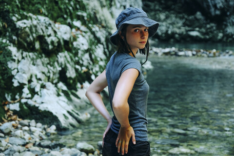 Portrait of woman wearing hat while standing at lakeshore against mountain stock photo